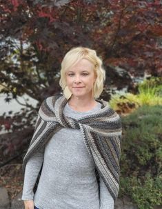 a woman standing in front of a tree wearing a gray sweater and blue jeans with her hand on her hip