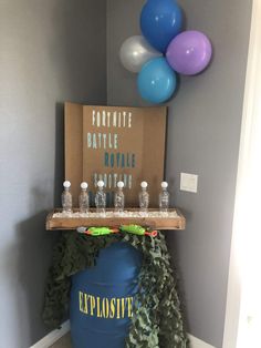 a table with balloons and bottles on it in the middle of a room next to a sign