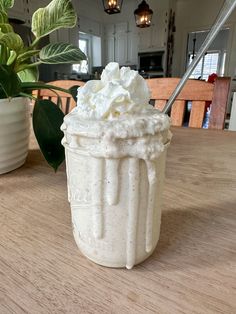 a cup filled with whipped cream sitting on top of a table next to a potted plant