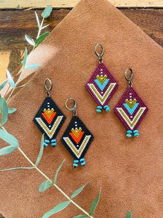 three pairs of beaded earrings sitting on top of a piece of cloth next to a plant