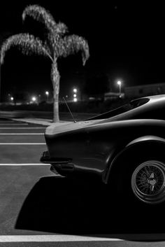 a black and white photo of an old car in a parking lot with palm trees