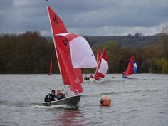 several small sailboats in the water with red and white sails, one being pulled by a boat