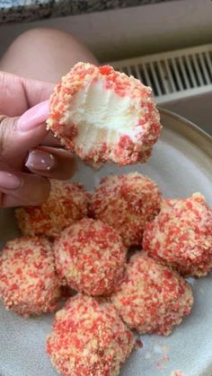 a person is holding up some food on a white plate with red sprinkles