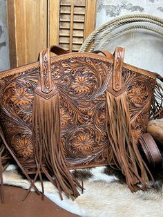 The Marfa Purse is a must-have for any fashion-forward individual. Crafted from tooled leather, this purse exudes luxury and sophistication. The leather fringe on the ends of the straps adds a touch of bohemian flair, making it perfect for any occasion. Make a statement with the Marfa Purse! Hand Tooled Western Bags, Western Leather Bag With Fringe, Western Brown Bag With Fringe, Brown Western Bag With Fringe, Traditional Fringe Bag, Luxury Brown Shoulder Bag With Tassels, Vintage Leather Bags With Fringe, Turquoise Accessories, Tooled Leather Handbags