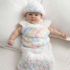 a baby laying on top of a bed wearing a knitted blanket and sleeping bag