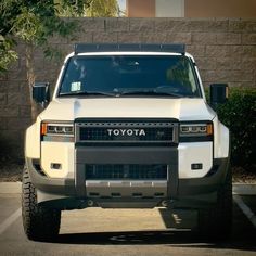 the front end of a white truck parked in a parking lot next to a brick wall