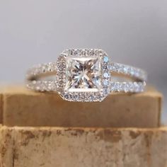 an engagement ring with a princess cut diamond surrounded by pave diamonds on a piece of wood