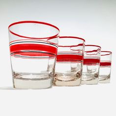 four red and clear glasses are lined up on a white surface, with one empty glass in the middle