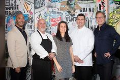 a group of people standing in front of a wall with graffiti on it and one person wearing an apron