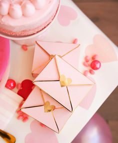 an origami box with hearts on it sitting next to a cake and balloons