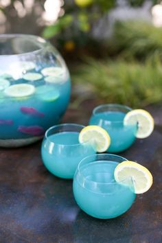 four glasses filled with blue liquid and lemons on a table next to a bowl