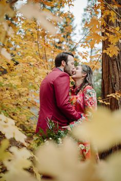 a man and woman standing next to each other in front of trees with yellow leaves