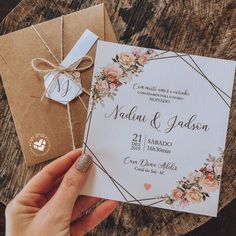 a person holding a wedding card in front of some brown envelopes with flowers on them