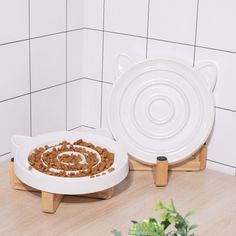 two plates with food in them sitting on wooden stands next to a potted plant