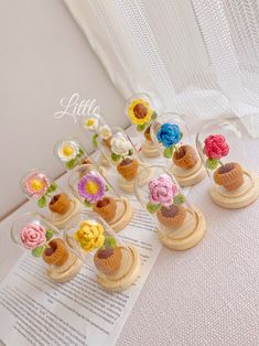 small crocheted flowers are in glass vases on top of an open book