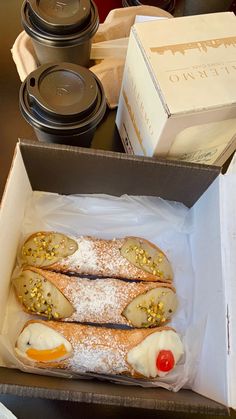 two hotdogs in a box with condiments on the table next to coffee cups