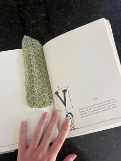 a person's hand is holding an open book with a crochet pattern on it