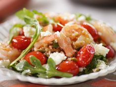 a salad with shrimp, tomatoes and feta cheese is on a white plate sitting on a table