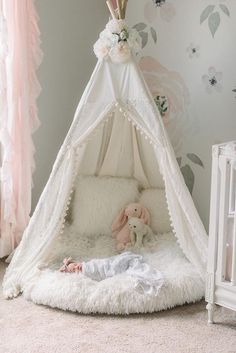 a baby's room with a teepee tent and flowers on the wall behind it