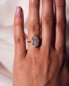 a woman's hand with a diamond ring on top of her finger and pink nail polish