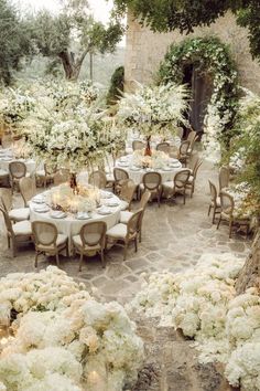 an outdoor dining area with tables, chairs and flowers on the table set for dinner