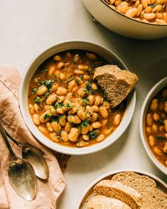 three bowls filled with beans and bread on top of a table