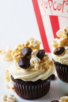 three cupcakes with white frosting and chocolate chips on top, next to a popcorn bag