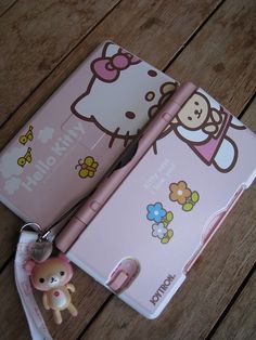 an open pink hello kitty notebook and keychain on a wooden table with a little doll