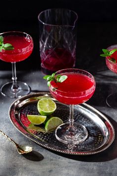 two glasses filled with red liquid and garnished with limes on a silver tray