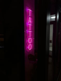 a neon sign that says tattoo on the side of a wall in a dark room