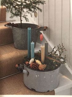 two buckets filled with pine cones and candles sitting on the steps next to a christmas tree