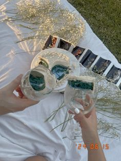 a woman is holding two glasses with green liquid in them on a white table cloth