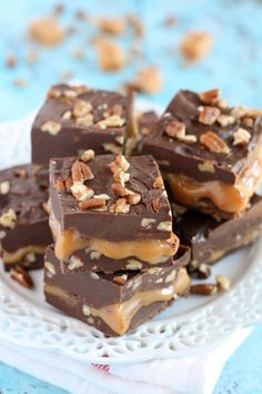 pieces of chocolate caramel fudge on a white plate with nuts and pecans