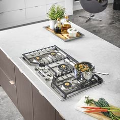 a kitchen counter with a stove and cutting board on it next to a potted plant