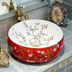 a red and white bowl sink sitting on top of a counter next to a mirror