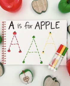 a is for apple book surrounded by apples and crayon pencils on white surface