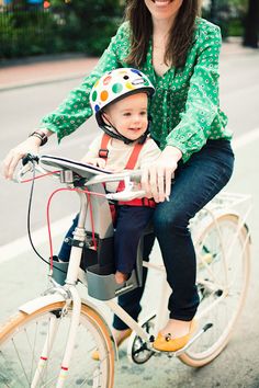 a woman riding a bike with a small child on the front seat and wearing a helmet