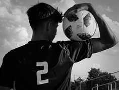 a young man holding a soccer ball in his right hand and looking at the sky