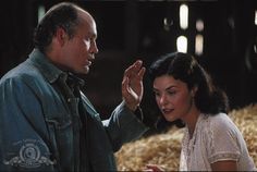 a man and woman standing next to each other in front of hay bales with their hands together