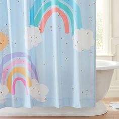 a shower curtain with rainbows and clouds on it in front of a bathtub