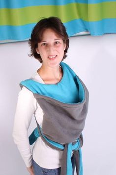 a woman is wearing a blue and gray wrap around her neck while standing in front of a white wall