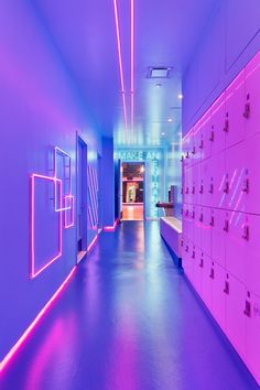 an empty hallway with lockers and neon lights on the walls in front of them