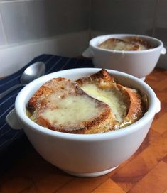 two bowls filled with bread and cheese on top of a wooden table next to a spoon