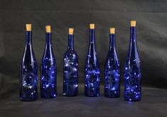 six blue glass bottles are lined up against a black background, each with a unique design on the top