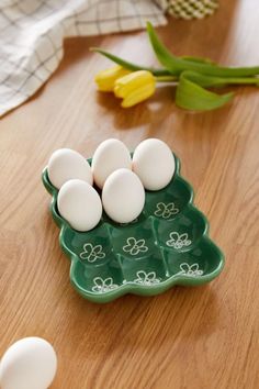 four eggs in a green tray on a wooden table next to tulips and flowers