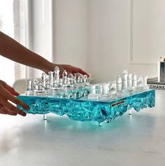 a person is playing chess on a blue plastic table with clear glass pieces in the foreground