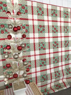 a red and white christmas tree is next to a plaid wall with ornaments on it