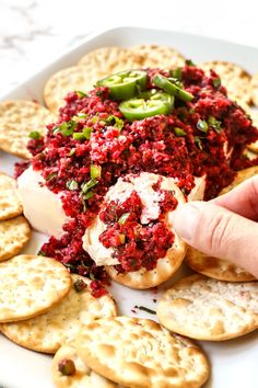 a plate with crackers, cheese and red sauce on it is being held up by a hand