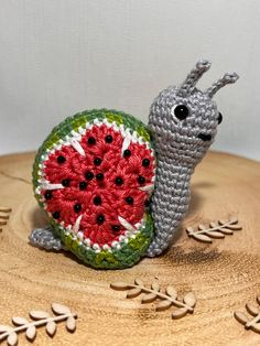 a crocheted snail sitting on top of a piece of wood next to a watermelon