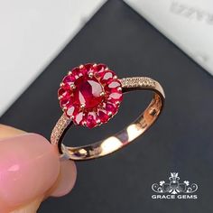 a person holding a ring with a red stone in it's center and diamond accents around the band